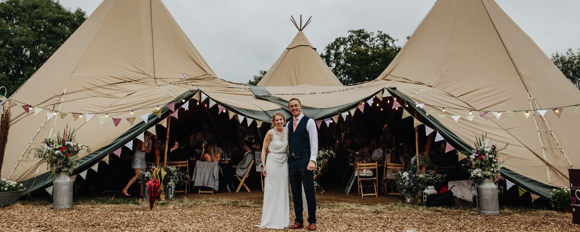 Wedding couple standing at the front of a three peaked festival tent